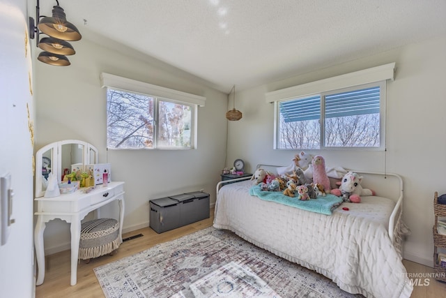 bedroom with visible vents, baseboards, a textured ceiling, and wood finished floors