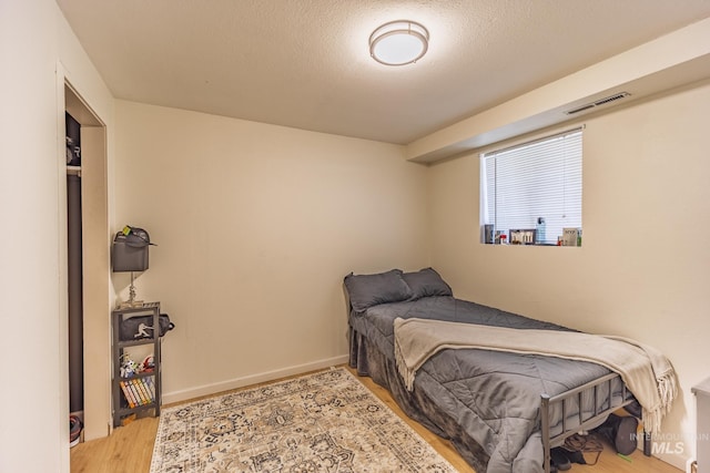 bedroom featuring visible vents, a textured ceiling, baseboards, and wood finished floors