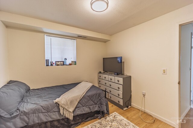 bedroom with a textured ceiling, wood finished floors, visible vents, and baseboards