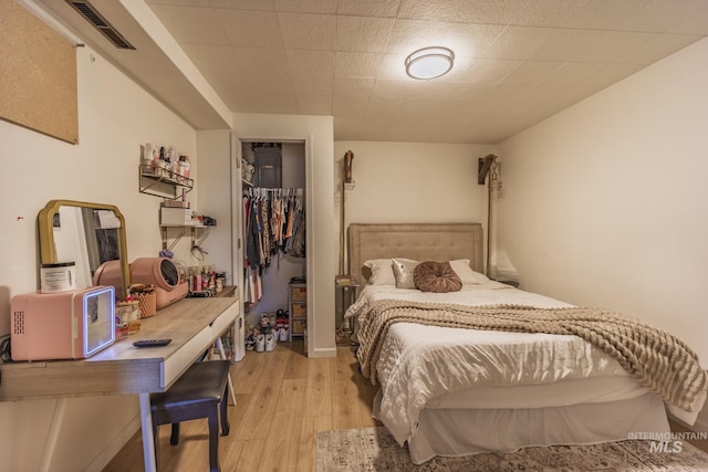 bedroom featuring light wood finished floors, visible vents, a walk in closet, and a closet