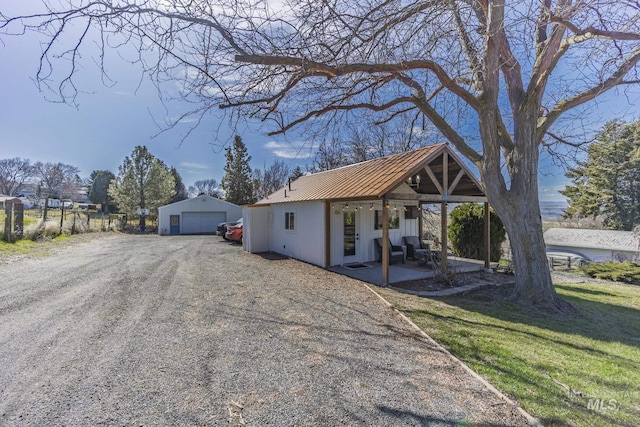 view of front of house with a patio, an outbuilding, a front yard, dirt driveway, and metal roof