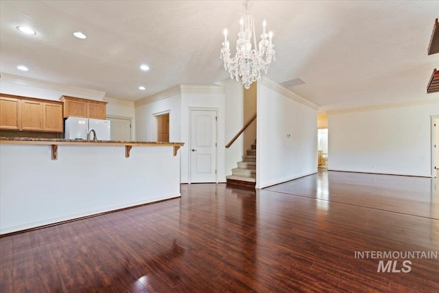 unfurnished living room featuring an inviting chandelier, crown molding, and dark hardwood / wood-style floors