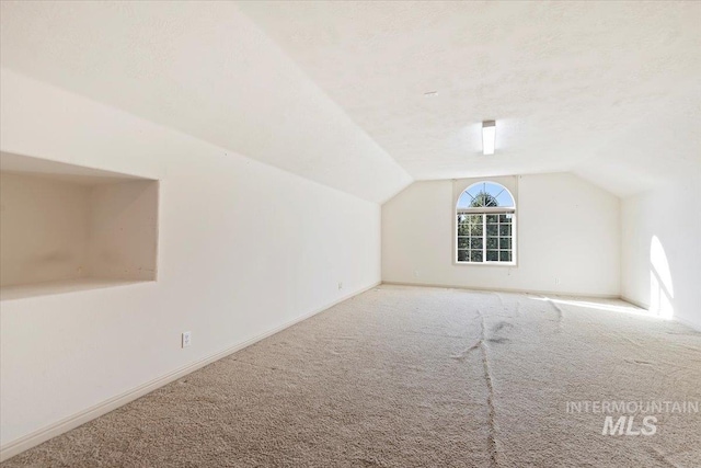 additional living space with carpet floors, vaulted ceiling, and a textured ceiling