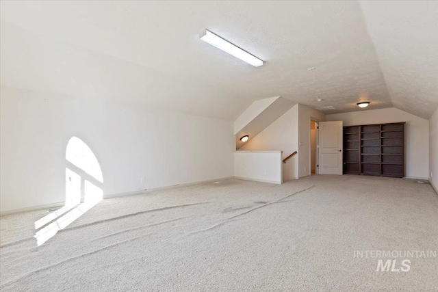 additional living space featuring lofted ceiling, light carpet, and a textured ceiling