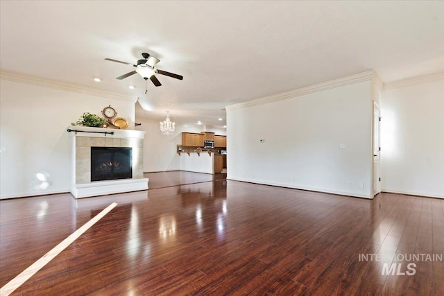 unfurnished living room featuring a tiled fireplace, crown molding, dark wood-type flooring, and ceiling fan with notable chandelier