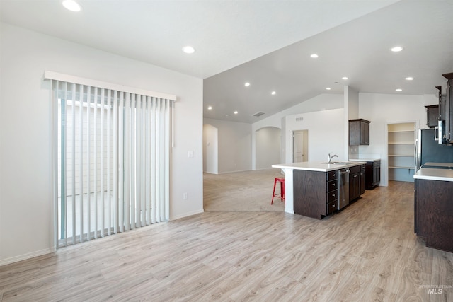 kitchen featuring light countertops, a kitchen breakfast bar, open floor plan, arched walkways, and dark brown cabinets