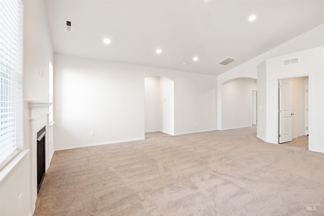 unfurnished living room featuring arched walkways, visible vents, and light carpet