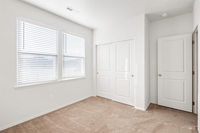 unfurnished bedroom featuring a closet, baseboards, visible vents, and light colored carpet