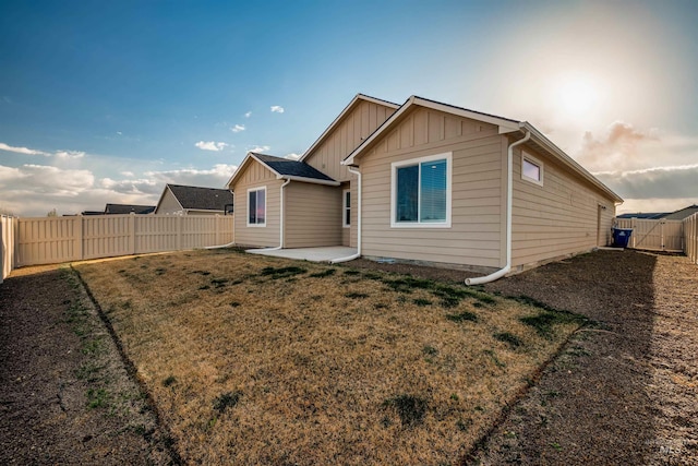 rear view of house with a fenced backyard, board and batten siding, a lawn, and a patio area