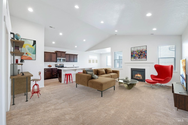 living room with visible vents, a glass covered fireplace, vaulted ceiling, and plenty of natural light