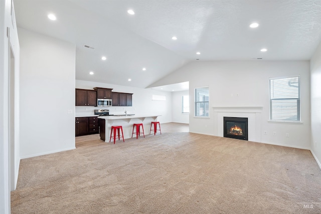 living area with visible vents, recessed lighting, light carpet, a glass covered fireplace, and vaulted ceiling
