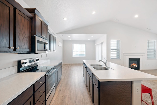 kitchen featuring light countertops, appliances with stainless steel finishes, lofted ceiling, a sink, and open floor plan