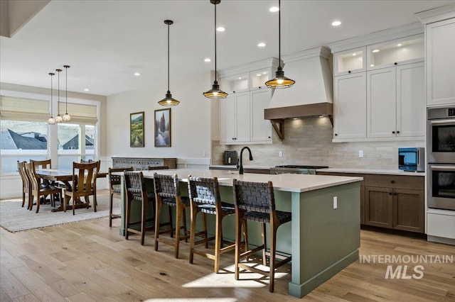 9351 W Sooty Grouse Ct, Boise, ID 83714 - kitchen with light countertops, decorative backsplash, light wood finished floors, a center island with sink, and premium range hood