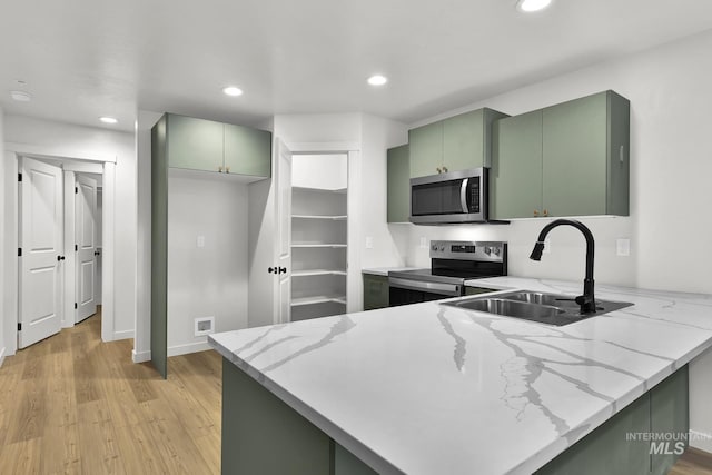 kitchen with green cabinetry, a sink, light wood finished floors, appliances with stainless steel finishes, and a peninsula
