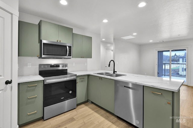 kitchen featuring a peninsula, stainless steel appliances, a sink, green cabinetry, and light wood-type flooring