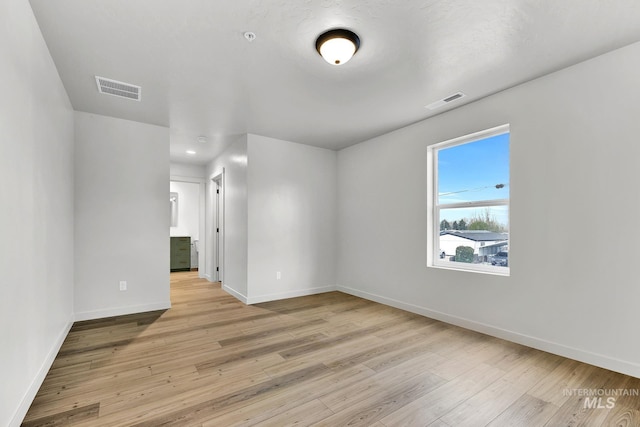 spare room with baseboards, light wood-type flooring, and visible vents