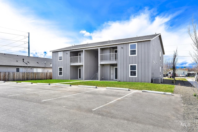 view of property featuring uncovered parking, cooling unit, fence, and stairway