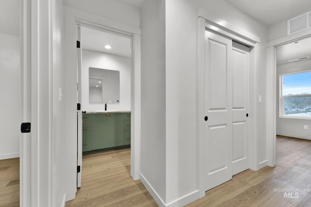 hallway featuring a sink, baseboards, light wood-style floors, and visible vents