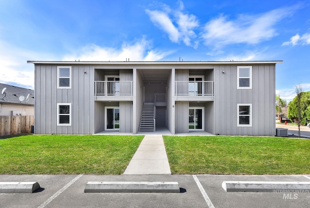 view of building exterior with fence, uncovered parking, stairway, and central AC unit
