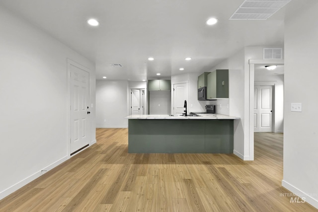 kitchen with light wood-type flooring, black microwave, visible vents, and a peninsula