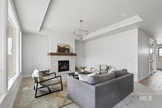 living area with a tray ceiling, a brick fireplace, baseboards, and a chandelier