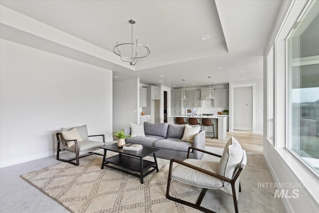 living room with a tray ceiling, recessed lighting, baseboards, and a chandelier