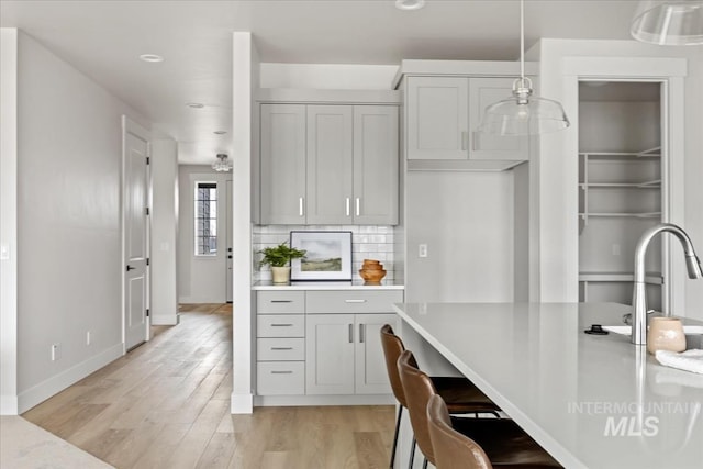 kitchen with backsplash, baseboards, light countertops, light wood-style flooring, and a sink