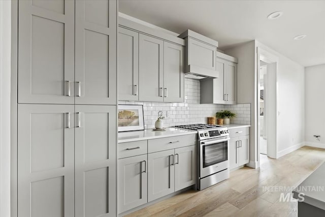 kitchen featuring light wood finished floors, light countertops, custom range hood, stainless steel gas range oven, and tasteful backsplash