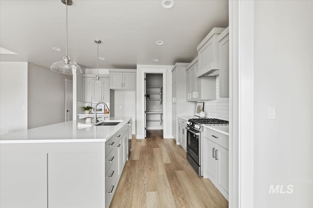 kitchen with light wood finished floors, light countertops, decorative backsplash, appliances with stainless steel finishes, and a sink