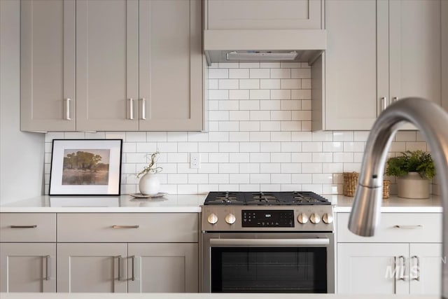 kitchen featuring decorative backsplash, stainless steel gas stove, exhaust hood, and light countertops