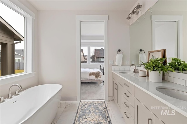 ensuite bathroom with a sink, a soaking tub, marble finish floor, and double vanity