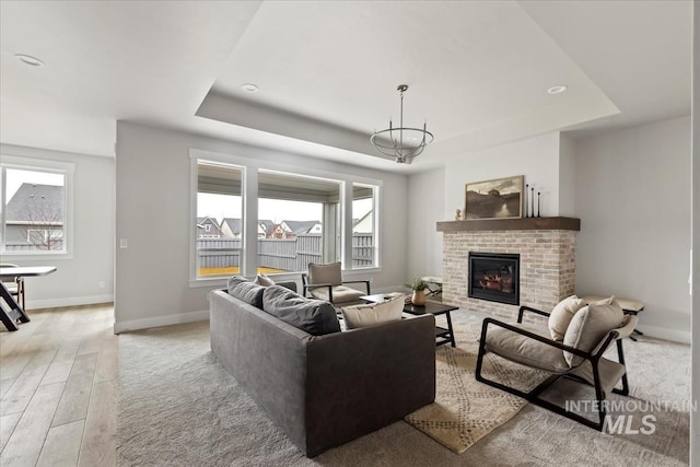 living room with a raised ceiling, a brick fireplace, and plenty of natural light