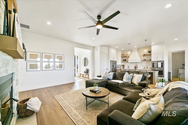 living room with a stone fireplace, a ceiling fan, and recessed lighting