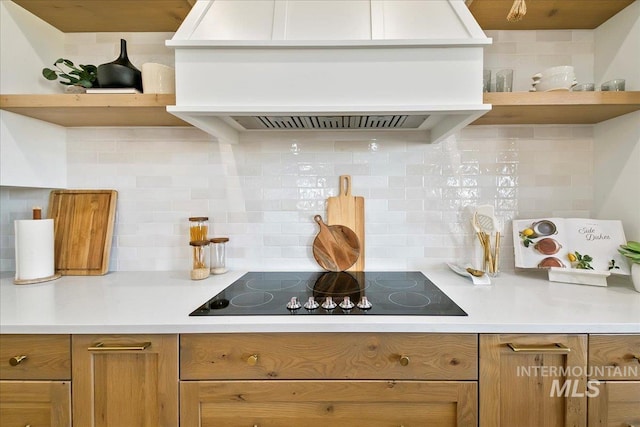 kitchen featuring custom exhaust hood, black electric stovetop, backsplash, open shelves, and brown cabinets