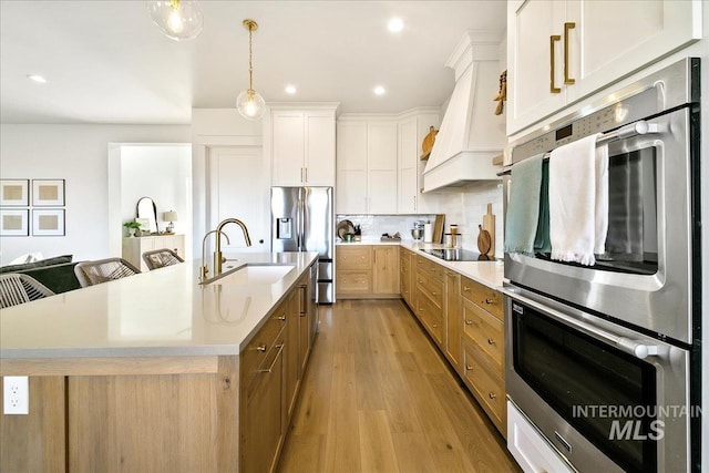 kitchen featuring light wood-style floors, appliances with stainless steel finishes, light countertops, a sink, and custom range hood