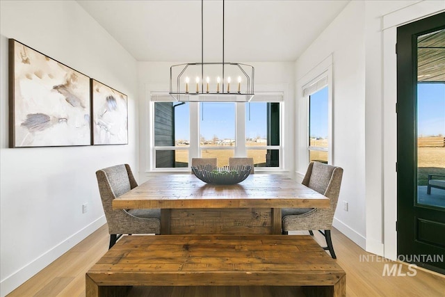 dining area with light wood-type flooring, baseboards, and an inviting chandelier