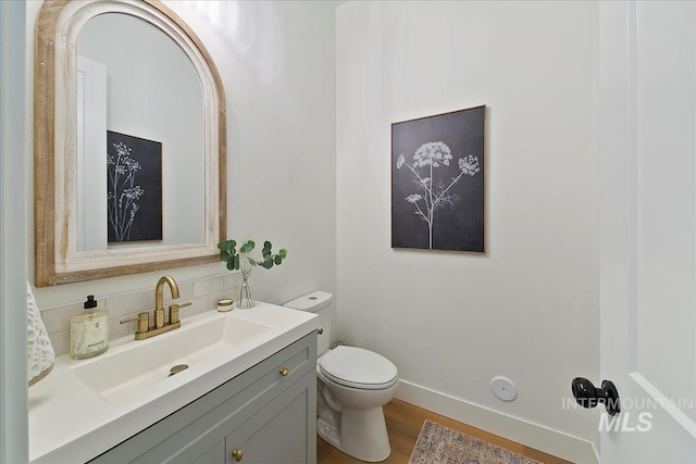 half bath featuring tasteful backsplash, vanity, baseboards, toilet, and wood finished floors