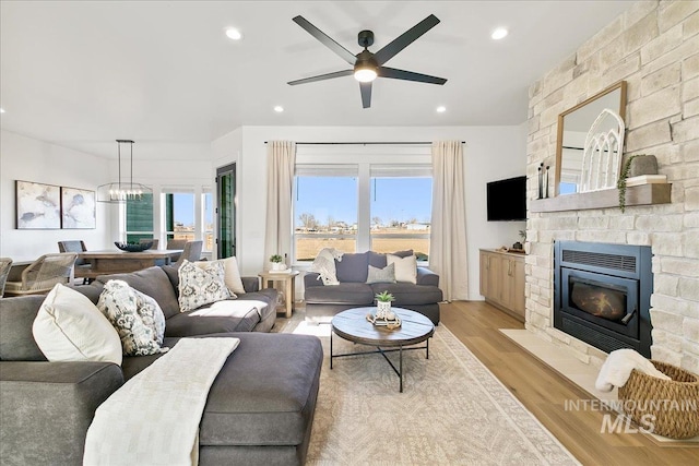 living room featuring ceiling fan with notable chandelier, light wood-type flooring, plenty of natural light, and a fireplace
