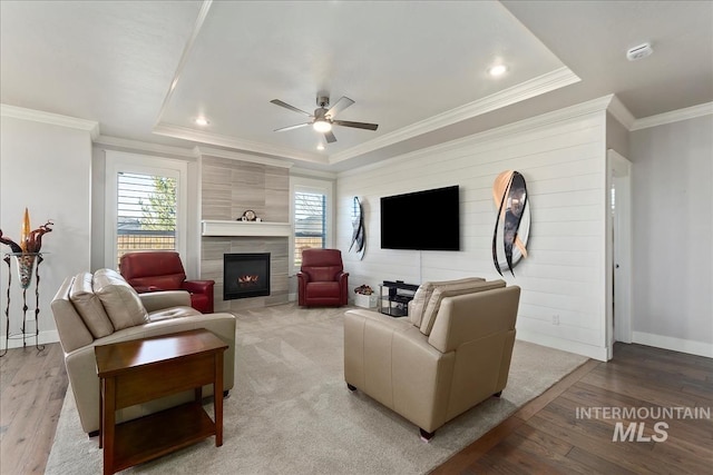 living room with a tile fireplace, ceiling fan, light hardwood / wood-style floors, a raised ceiling, and crown molding