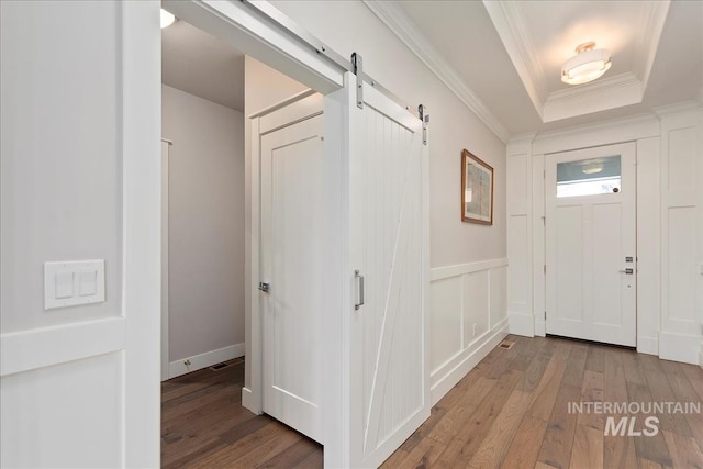 entryway with crown molding, a barn door, a raised ceiling, and light hardwood / wood-style floors