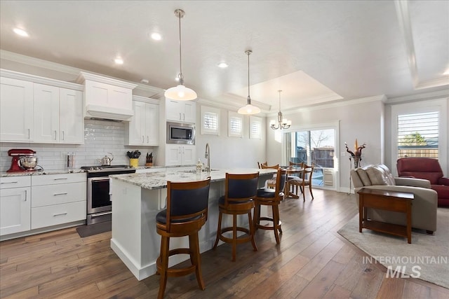 kitchen with a breakfast bar, decorative light fixtures, a center island with sink, stainless steel appliances, and white cabinets