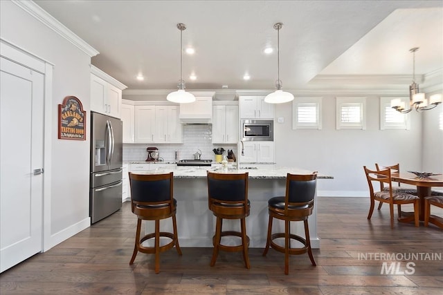 kitchen featuring pendant lighting, crown molding, appliances with stainless steel finishes, white cabinetry, and a kitchen island with sink