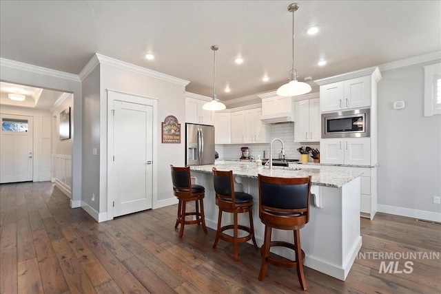 kitchen featuring appliances with stainless steel finishes, light stone counters, white cabinets, a center island with sink, and decorative light fixtures