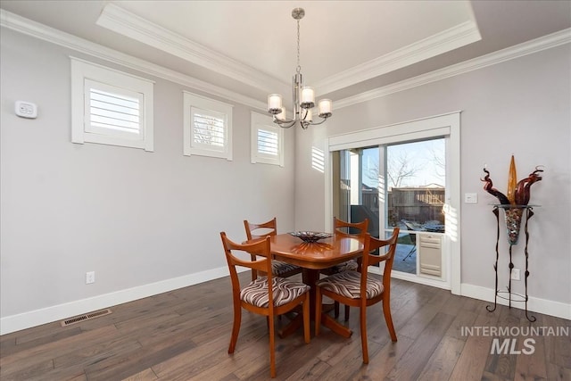 dining room featuring crown molding, dark wood-type flooring, an inviting chandelier, and a tray ceiling