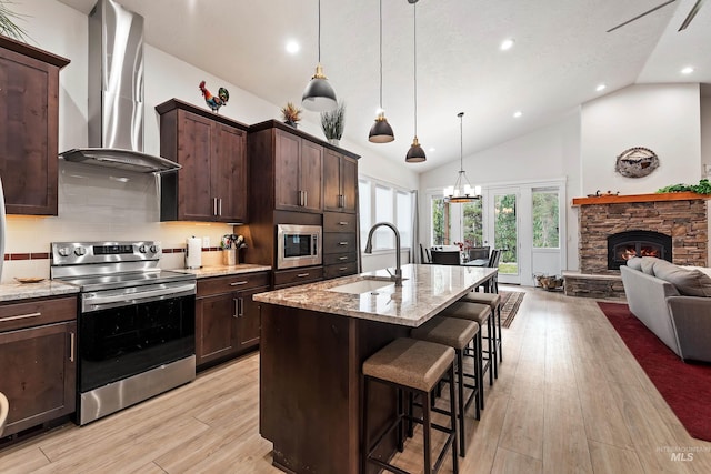 kitchen with wall chimney range hood, sink, stainless steel appliances, light stone countertops, and decorative light fixtures