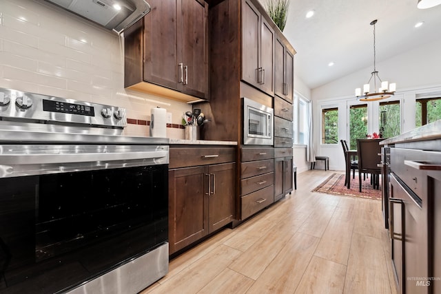 kitchen with pendant lighting, backsplash, stainless steel appliances, wall chimney exhaust hood, and light wood-type flooring