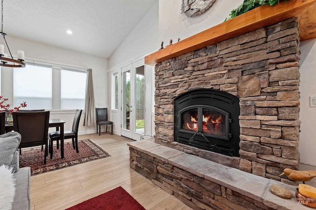 living room featuring lofted ceiling, a stone fireplace, and light wood-type flooring