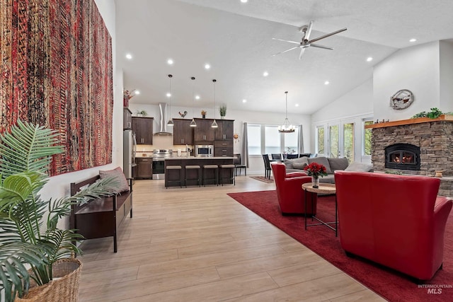 living room featuring a stone fireplace, ceiling fan with notable chandelier, high vaulted ceiling, a textured ceiling, and light hardwood / wood-style flooring