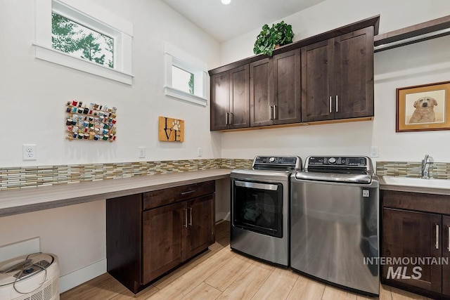 laundry area with sink, light hardwood / wood-style flooring, washing machine and dryer, and cabinets