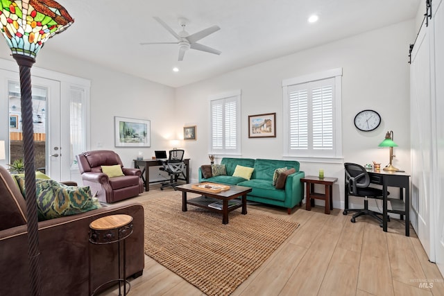 living room with light hardwood / wood-style flooring, a barn door, ceiling fan, and french doors